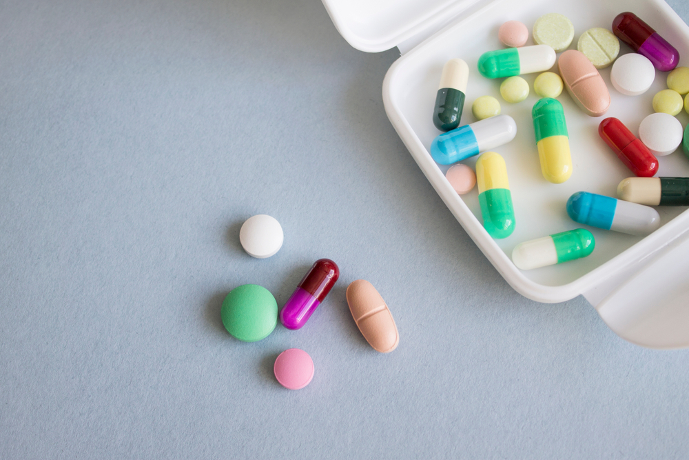 White box-container of multiple colors pills over grey-blue background. Package of pills on a gray background.