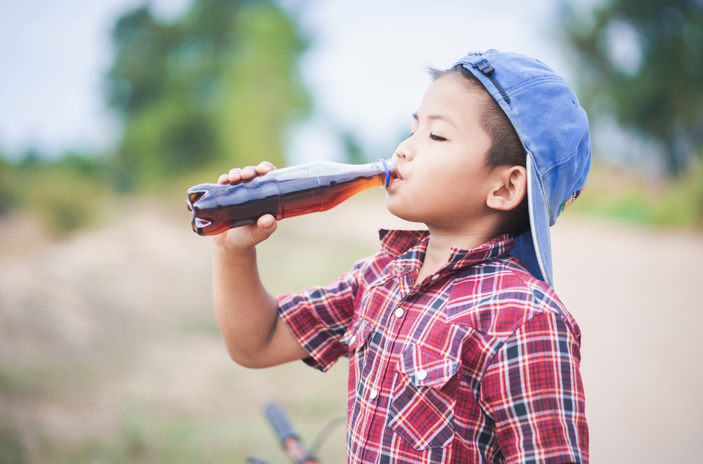 Little boy drinking sparkling water bottle after mini cycling.