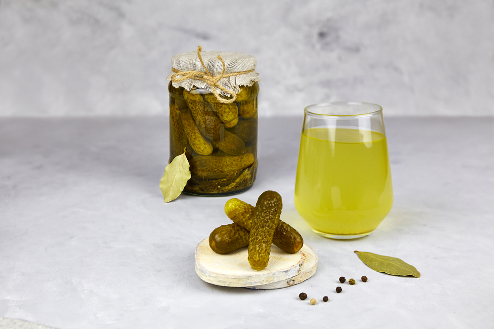 Pickled cucumbers in a glass jar and pickle juice in glass on a light background. Homemade fermented or marinated cucumbers. Healthy energy drink for athletes.