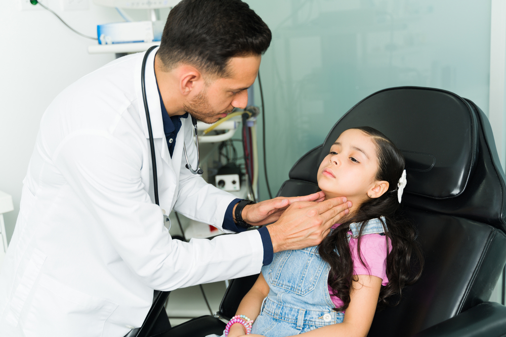 Otolaryngologist doctor examining a little girl. Sick elementary kid lying on the examination chair and getting diagnosed with strep throat

