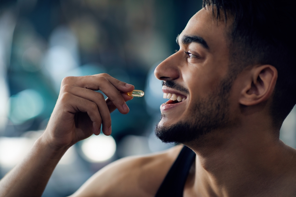 Portrait Of Happy Sportive Arab Man Taking Supplement Capsule, Closeup Shot Of Young Middle Eastern Guy Eating Omega 3 Or Amino Acid Multivitamin Pill, Enjoying Fitness Nutrition, Cropped