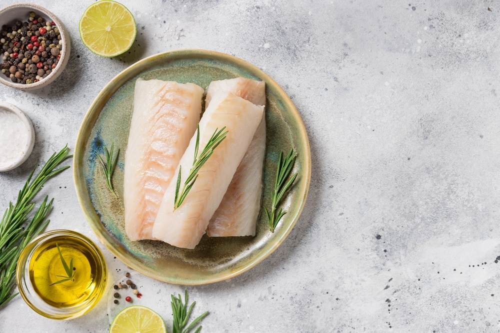 seafood background with ingredients for cooking. Raw cod loin fillet steak with aromatic herbs, spices, lime and olive oil on kitchen table. space for text