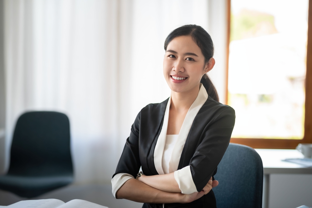 Beautiful smiling Asian businesswoman sitting with arms crossed looking at camera in the office.
