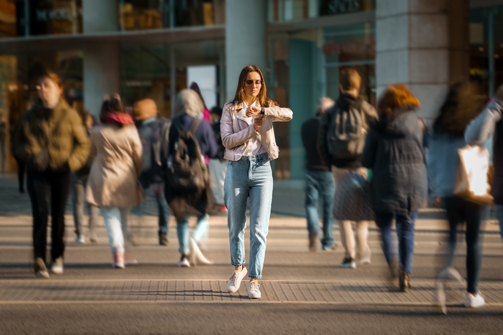 Young woman walking in the middle of crowded street and looking time at hand watches. Big city life.