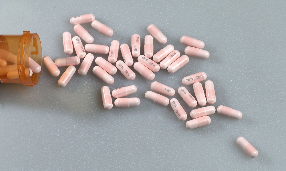 Three hundred milligram pink Lithium Carbonate capsules spilling out of a prescription drug container onto a white surface.