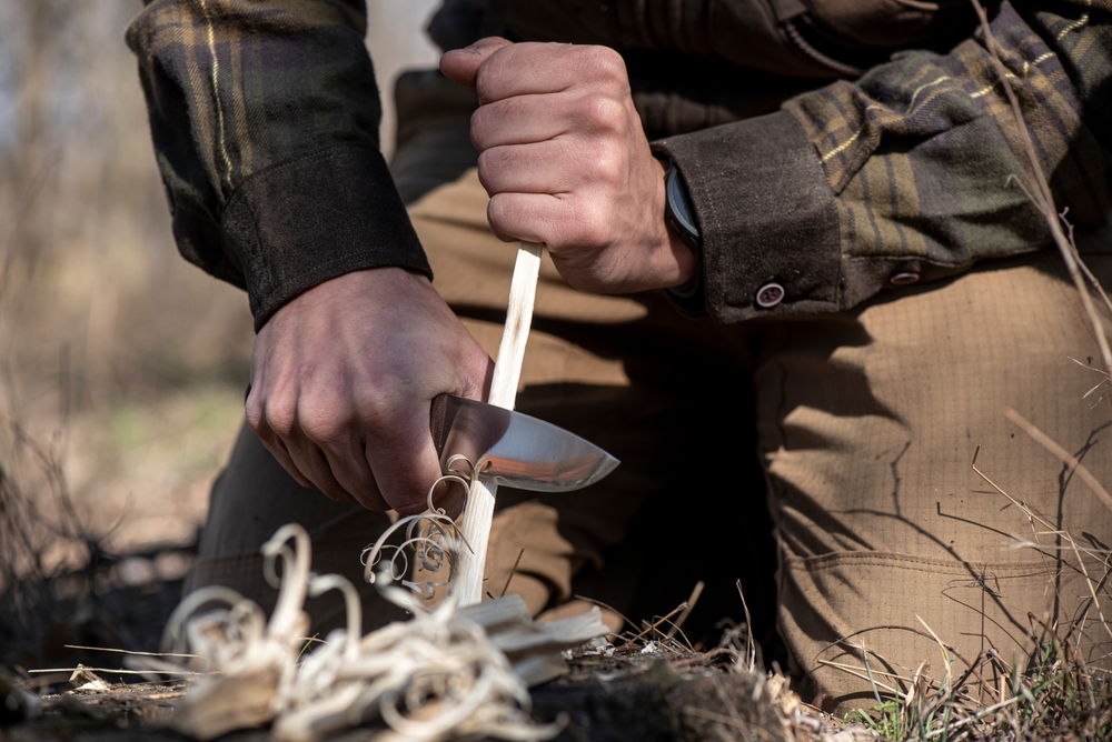 Bushcraft man making feather stick with knife to start fire