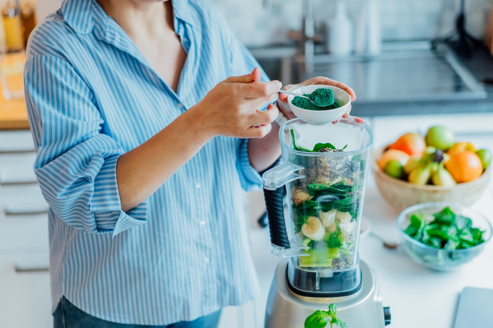 A woman adds Spirulina Green Powder while making a green smoothie in the kitchen. Superfood supplement. Healthy Detox Vegan Diet. Healthy diet, weight loss program. Selective focus.
