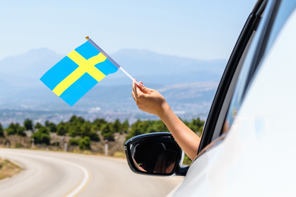 Woman holding Sweden flag from the open car window driving along the serpentine road in the mountains. Concept