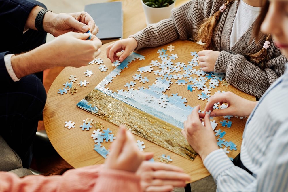 Close up of unrecognizable family playing jigsaw puzzle game together at home