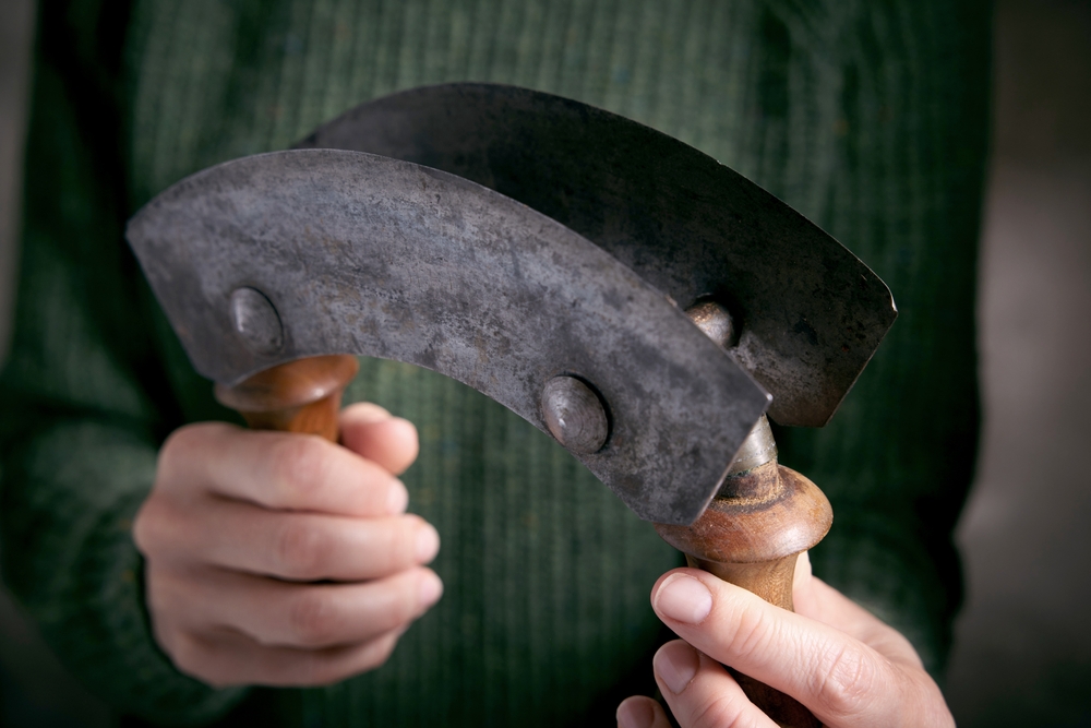 Crop anonymous female holding traditional sharp metal old fashioned double bladed mezzaluna knife with wooden handles