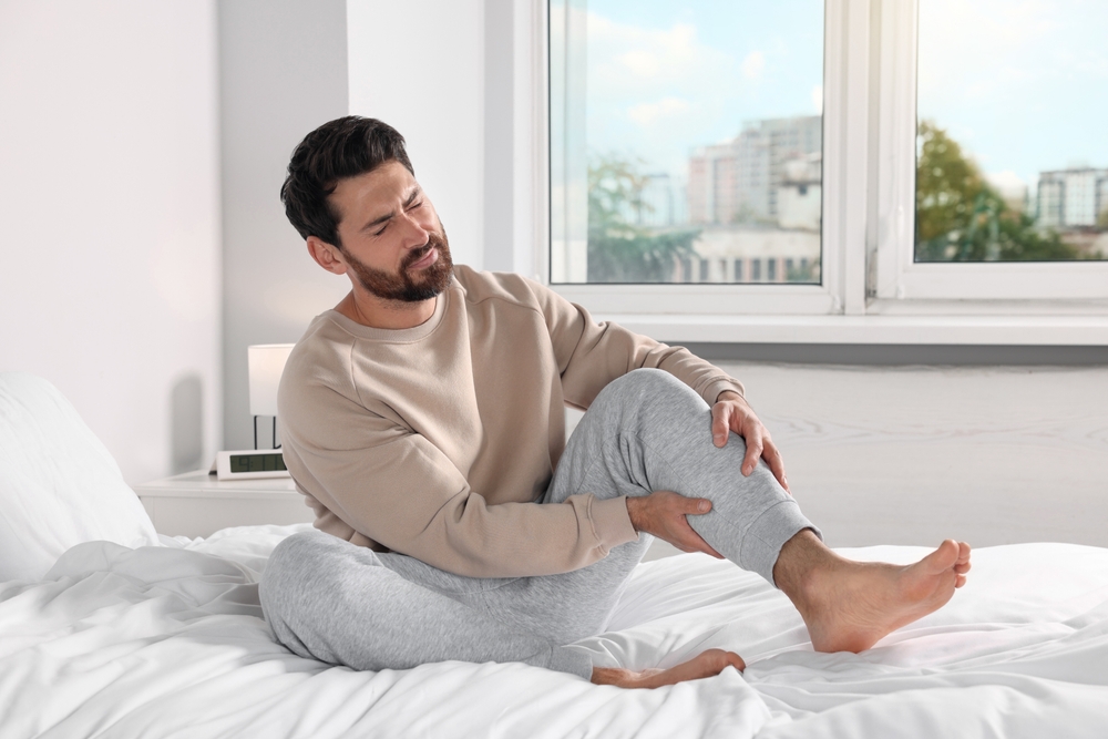 Man suffering from leg pain on bed at home
