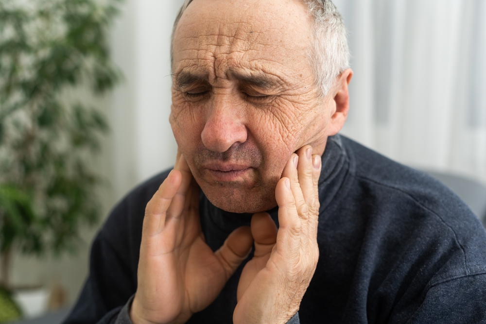 Old man with toothache. Elderly senior man has toothache. Unhappy man face in tooth pain sitting on sofa at home, feel sick unwell. Sad aged man hand holding his chin. Adult suffering toothache