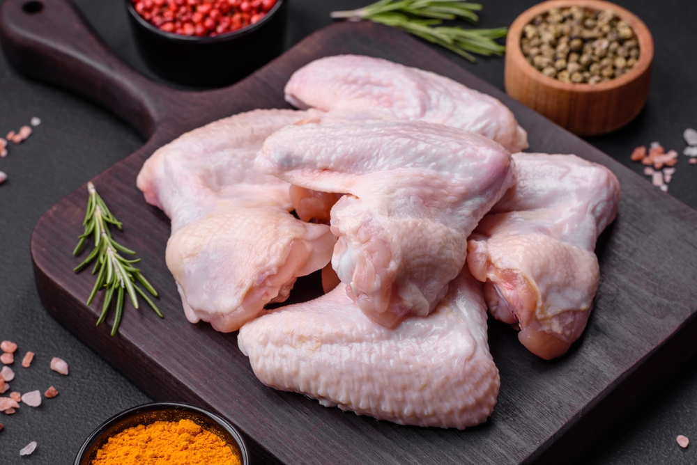 Raw chicken wings with salt, spices and herbs on a wooden cutting board on a dark concrete background