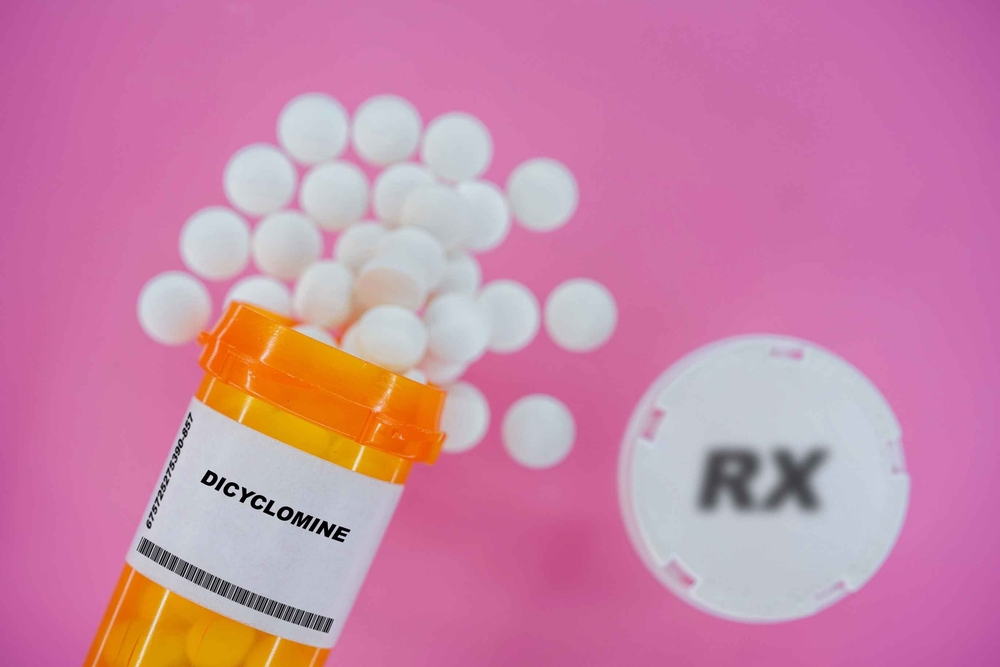 Dicyclomine Rx medicine pills in plactic vial with tablets. Pills spilling   from yellow container on pink background.