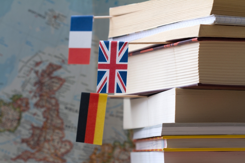 Stack of books with country flags on background of map, foreign language learning concept