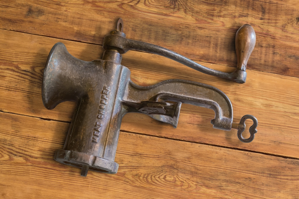 Old vintage hand-powered meat chopper assembled for use lying on the rustic table

