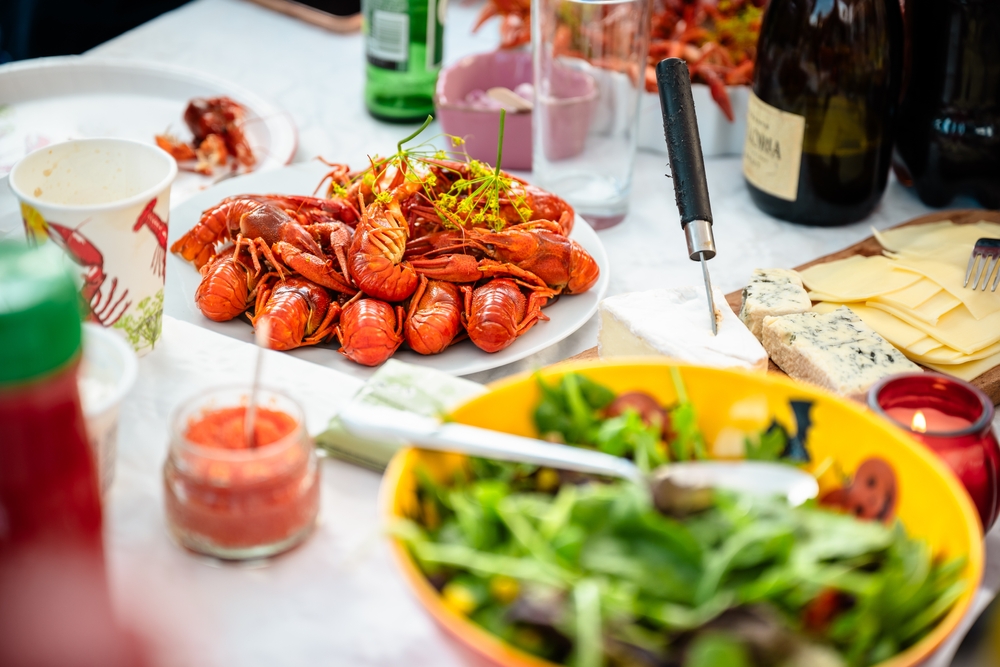 set table with a platter of boiled crayfish and various cheeses, salad and drinks all around