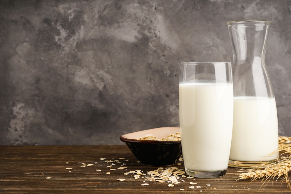 Oat milk in the glass with jug of milk and oat on a wooden background. The concept of a vegetarian diet.