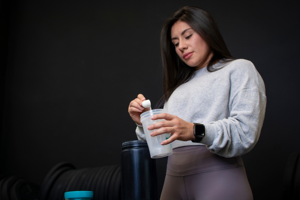 Female athlete preparing her protein in a shaker prior to weight training