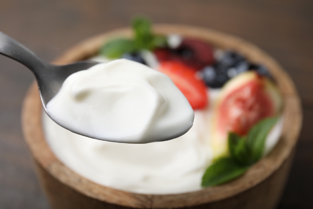 A spoonful of delicious yogurt is on a bowl on the table, nearby. Text space