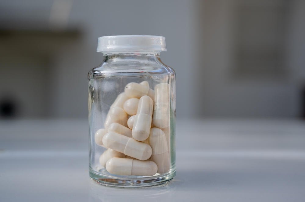 A glass jar with white pills or capsules on a blurred background