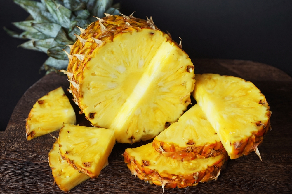 Ripe juicy pineapple next to cut pieces on a wooden board on a dark background