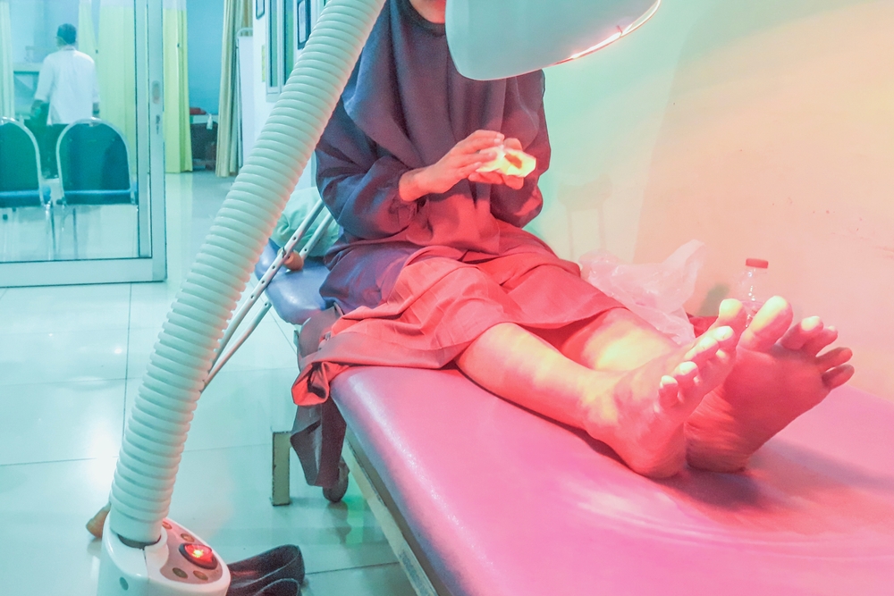 Young woman sitting undergoing infrared radiation therapy for pain treatment in clinic