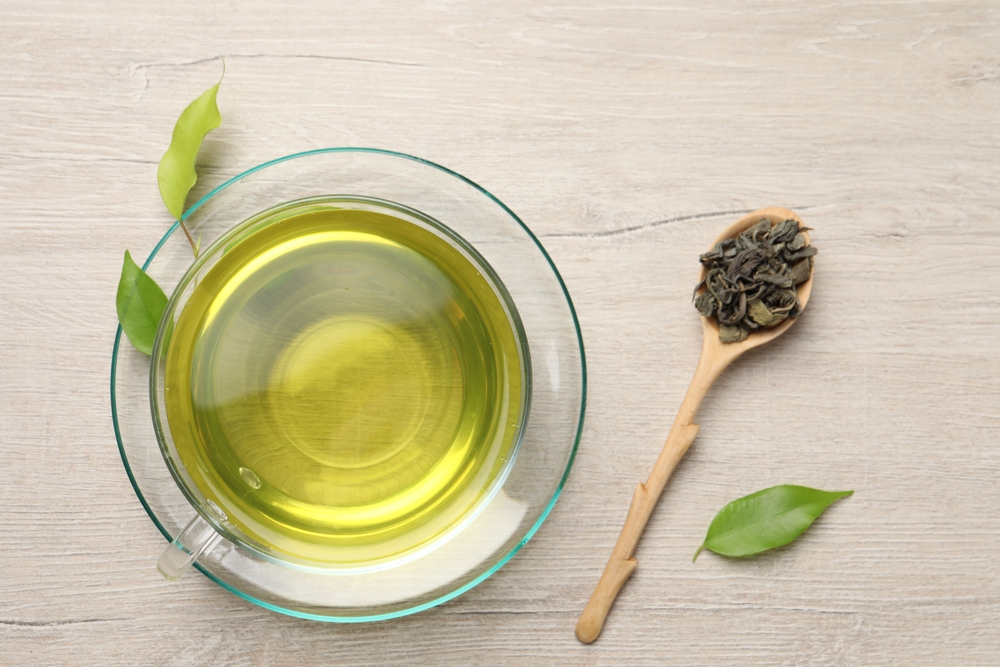 Refreshing green tea in cup, spoon and leaves on wooden table, apartment