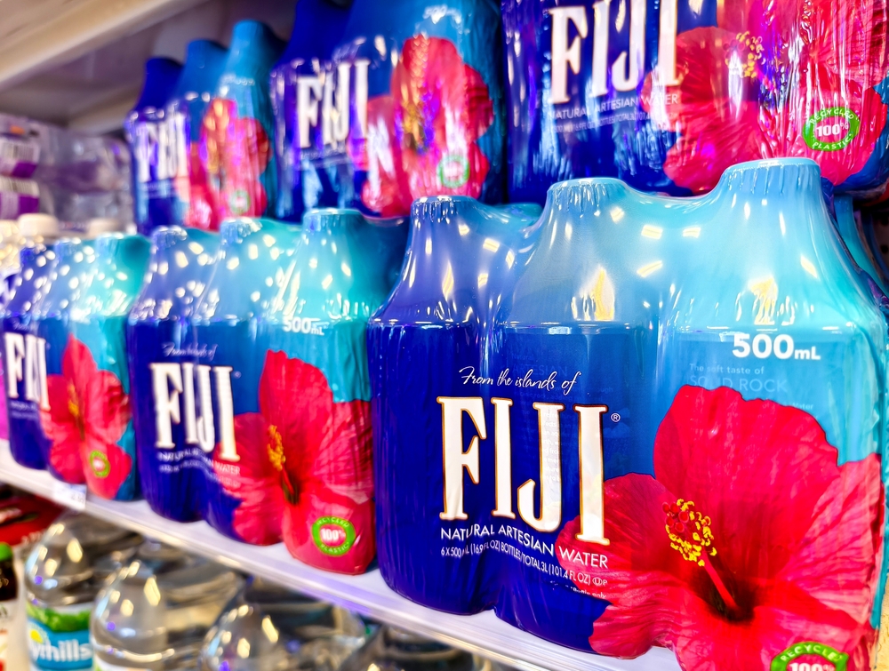 Florida - June 25, 2024: Close-up of bottled Fiji water packs on a supermarket shelf. Vibrant blue packaging with red flower branding.