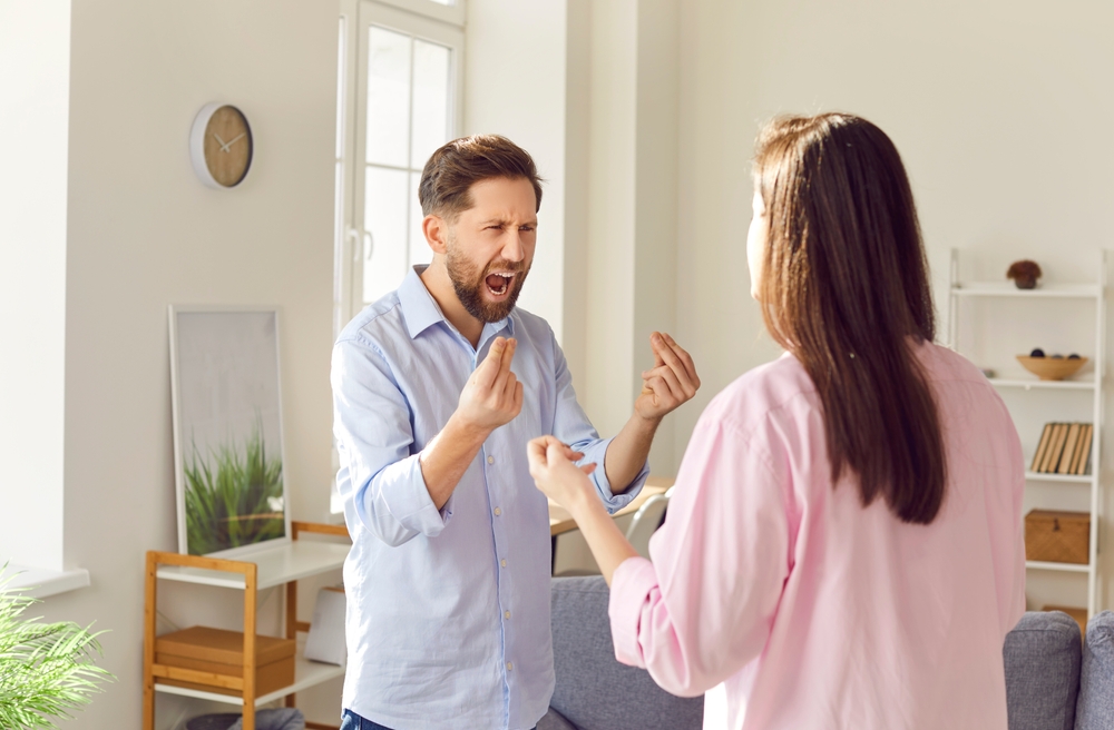 Young couple man and woman standing at home and arguing shouting in quarrel. Angry unhappy husband and wife quarreling in the living room. Marriage problems, relationship and divorce concept.