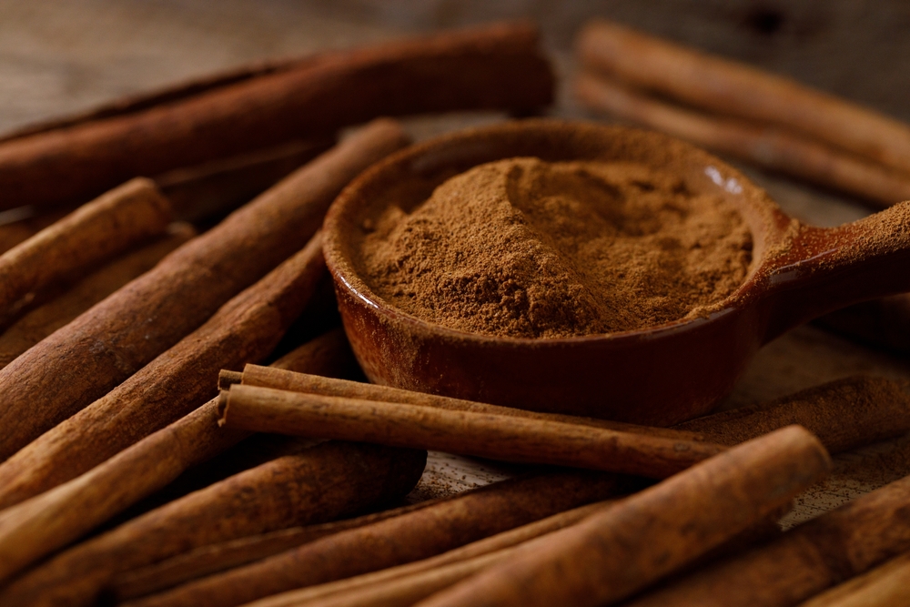 Cinnamon sticks and cinnamon powder on dark rustic background. Closeup.