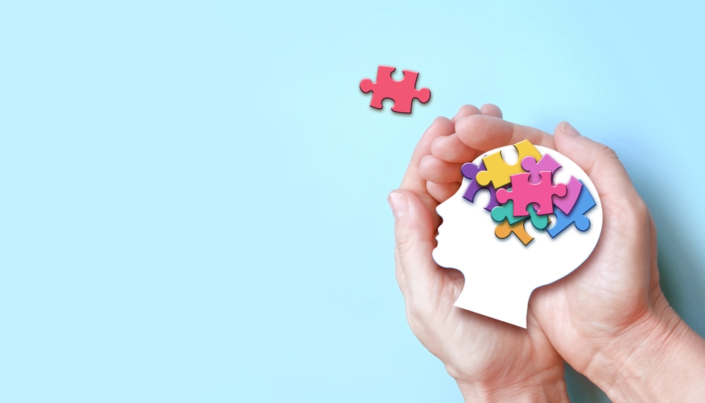 Hands holding paper head with jigsaw puzzle, Autism spectrum disorder family support concept, World Autism Awareness Day.