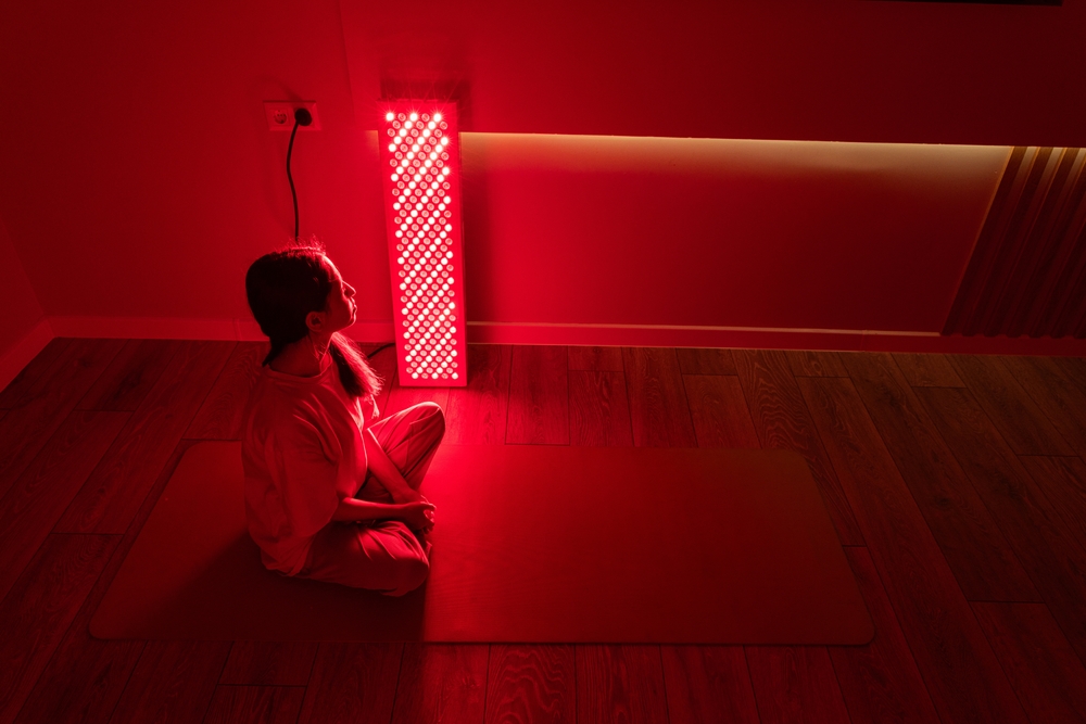 A young woman meditating indoors illuminated by red light therapy equipment