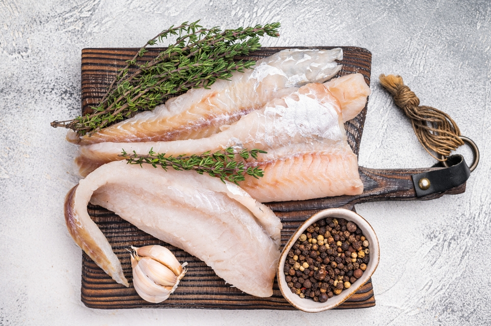 fresh Raw Pollock fish fillets on a wooden board with herbs. white background. top view.