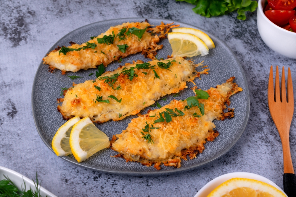 Flounder fillet baked in a parmesan crust, served with lemon wedges on a ceramic plate. How to cook white fish
