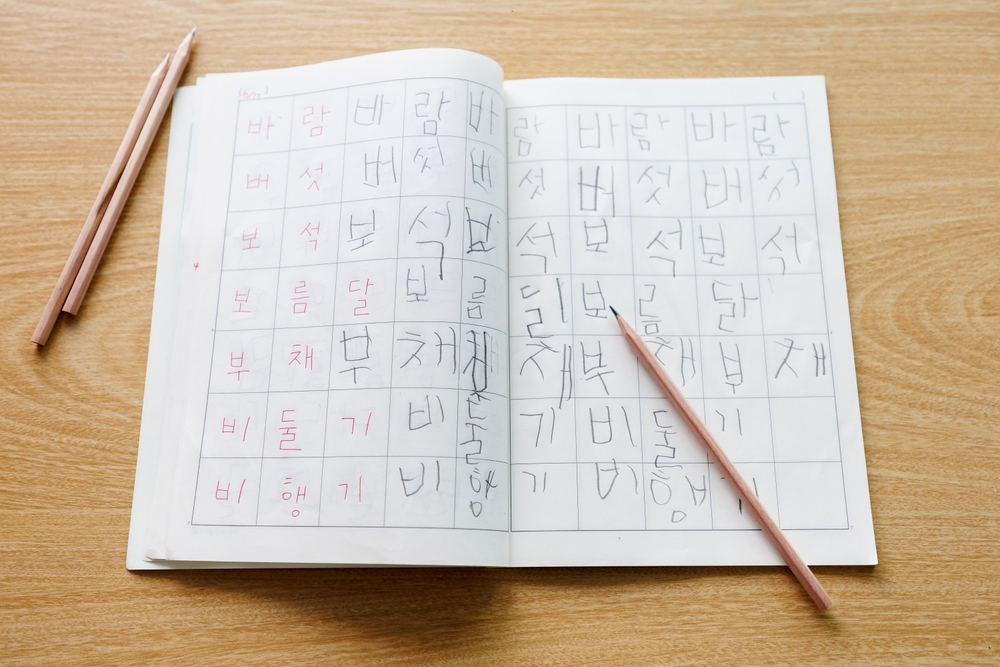 Open Korean handwriting workbook with Hangul alphabet practice sheets and pencils on wooden desk. Concept of studying Korean language, education, calligraphy, student learning materials