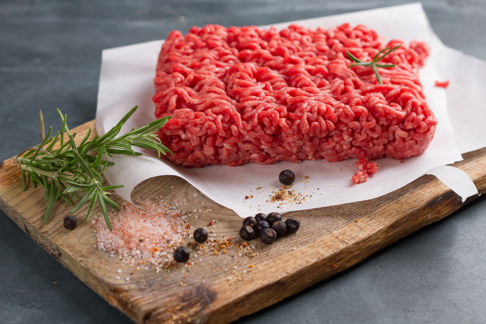 Minced meat on butcher paper with basil and pepper, selective focus