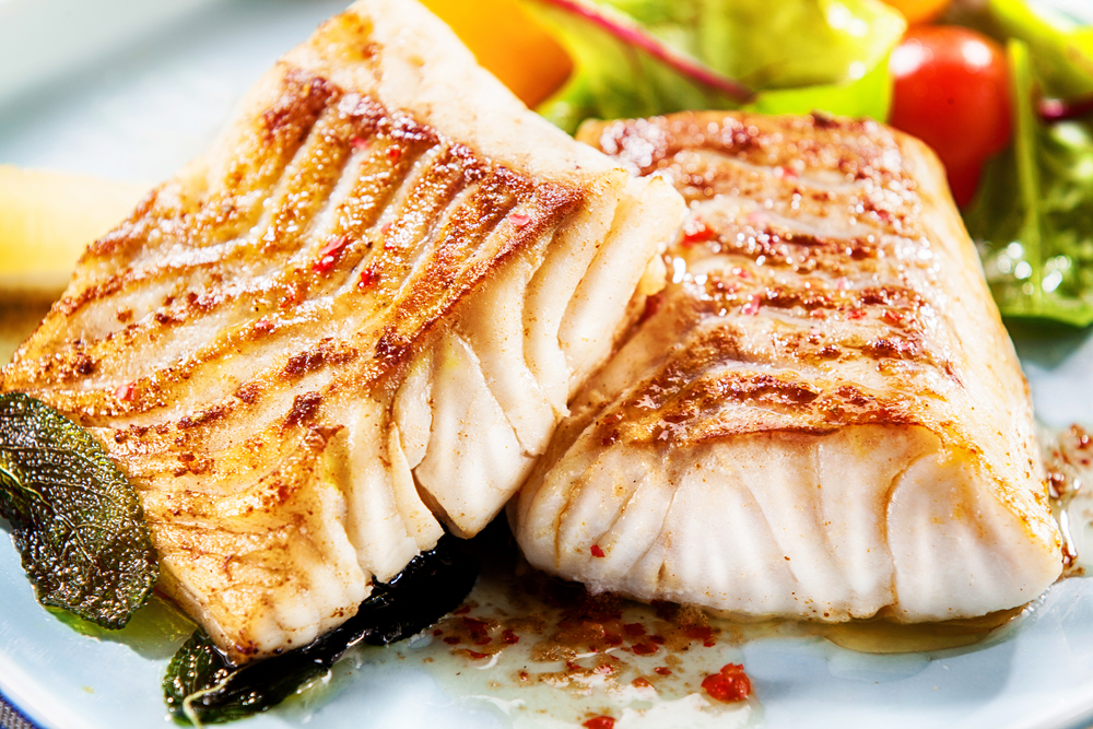 Two delicious fillets of marinated grilled or oven baked pollock or coalfish served with a fresh salad, close up view showing the texture