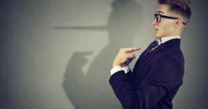 Man pointing at himself in disbelief, a shadow of humself cast on background with long Pinocchio type nose. Liar concept