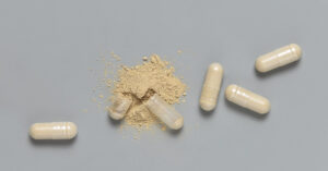 Top Supplement Mistakes You're Probably Making, Backed by Nutrition Science Medical capsules with opened one to show beige powder on grey top view. Preventive medicine and healthcare, taking alternative dietary supplements and vitamins