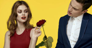 How Narcissists Express 'Love': 3 Psychology-Backed Patterns to Know Man offering a rose to a woman wearing a red dress. Yellow background