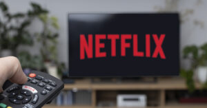 Person pointing TV remote with Netflix displayed on it.