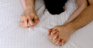 Why Sex Can Trigger Emotional Attachment, According to Psychology two people holding hands with their fingers interlocked. This type of hand-holding is often seen as a sign of a strong emotional connection and intimacy between two people