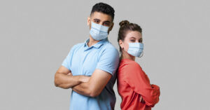 How COVID Might Be Affecting Male Fertility and the Health of Future Children Man and Woman standing back to back with arms crossed while wearing PPE face masks