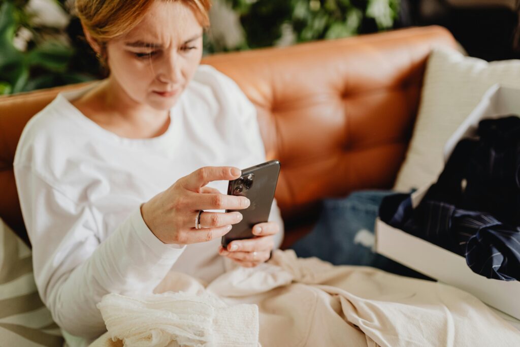 Woman with furrowed brow looking down at smartphone while sitting on couch.