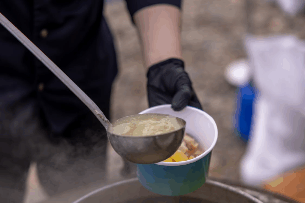 Person serving hot soup outdoors with ladle