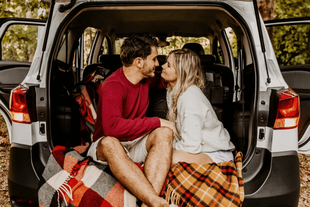 man and woman sitting on blanket in back of van