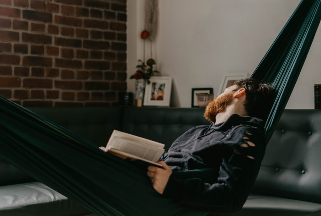 Person reclining in hammock reading book in living room with brick wall behind them.