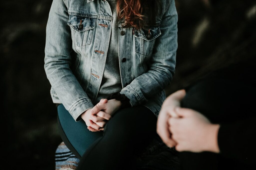 Woman with hands held tightly in lap sitting across from another person.