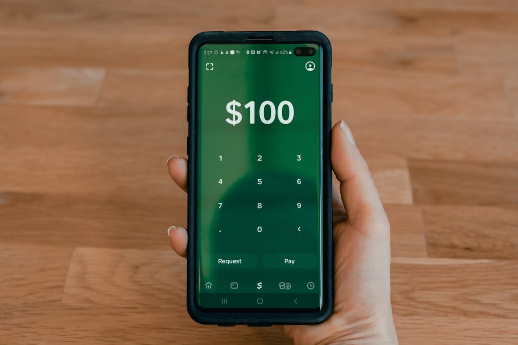Hand holding smartphone displaying cash payment app with $100 amount.